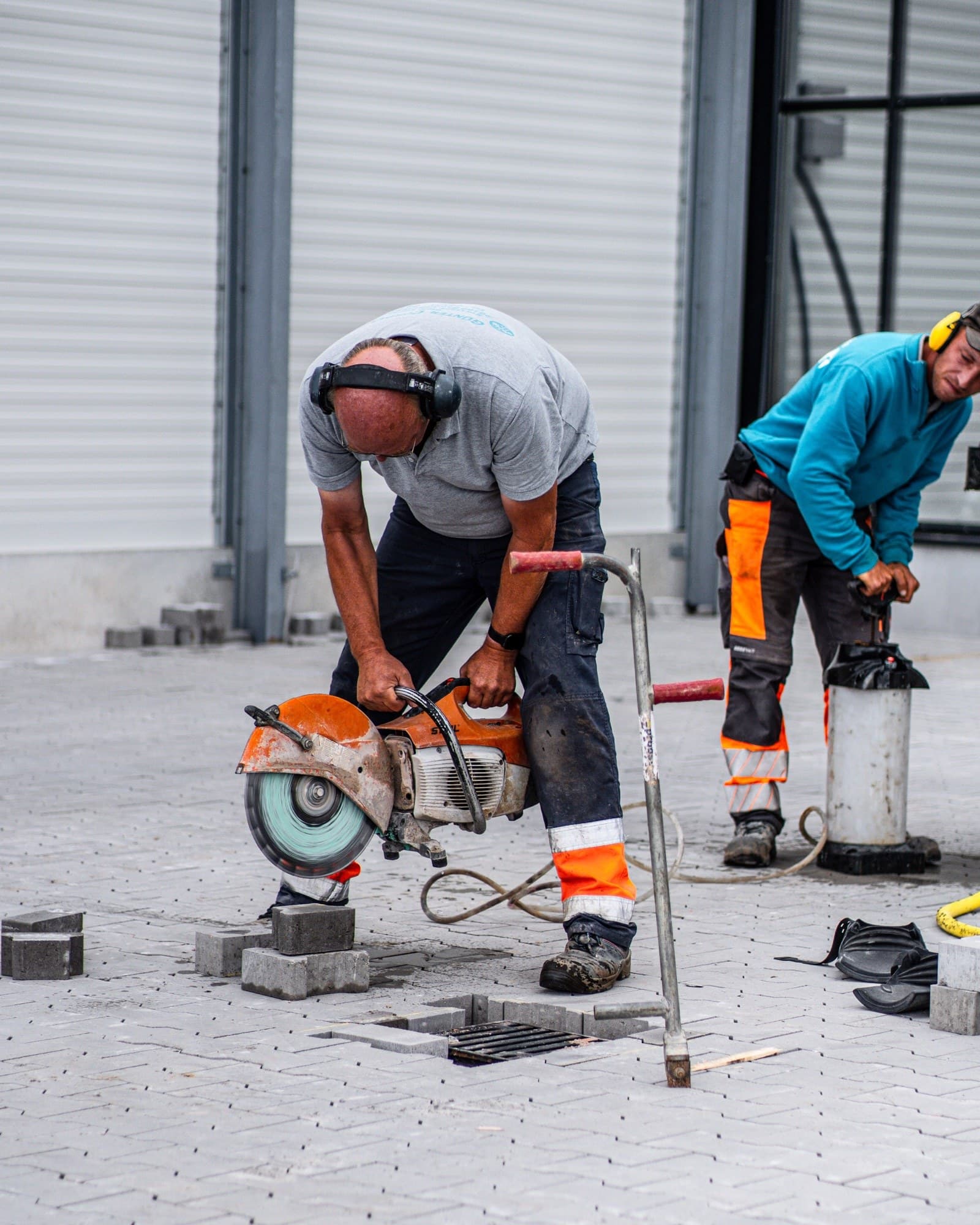 Zwei Mitarbeiter der Günter Cordes GmbH beim Trennschneiden von Pflastersteinen auf einer Baustelle, einer im Cordes-Shirt